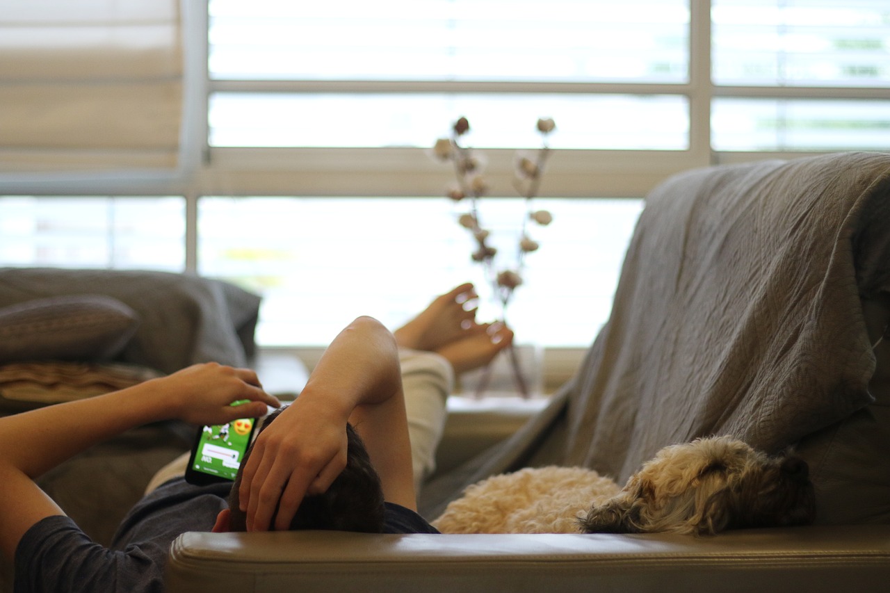Man lying on the sofa with his smartphone, his dog lying next to him