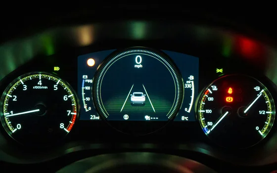 Beleuchtetes Armaturenbrett eines Autos bei Nacht. In der Mitte zeigt ein digitales Display 0 mph und eine Spurhaltegrafik. Links ist ein Drehzahlmesser und rechts Analoganzeigen für Kraftstoff und Motortemperatur zu sehen.