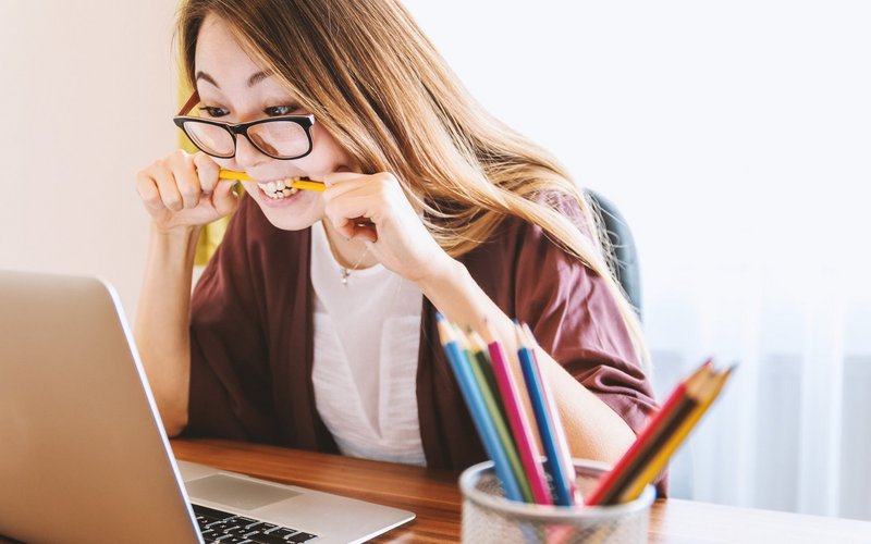 Young woman bites pencil in despair, sitting in front of screen