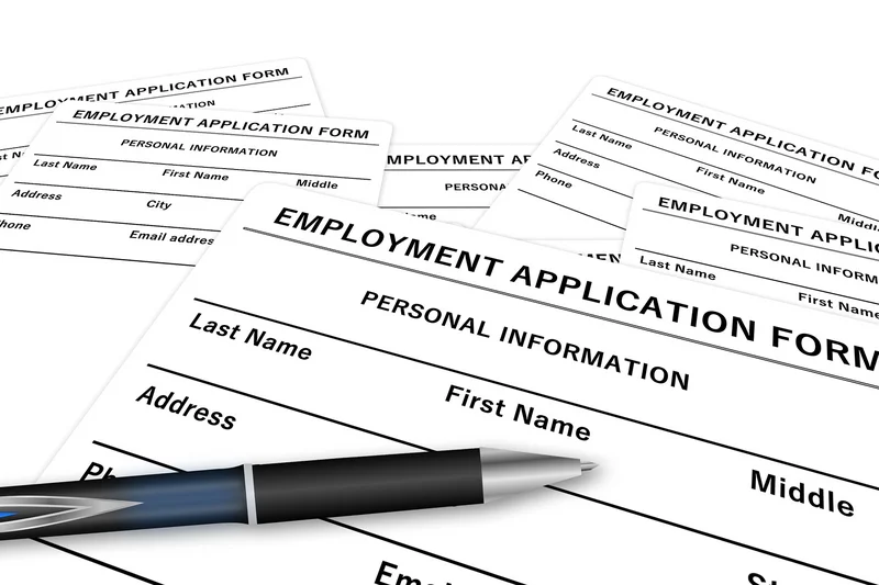 The image shows multiple employment application forms with sections for personal information such as last name, first name, middle name, address, phone number, and email address. A pen is placed on top of the forms, indicating readiness to fill them out.